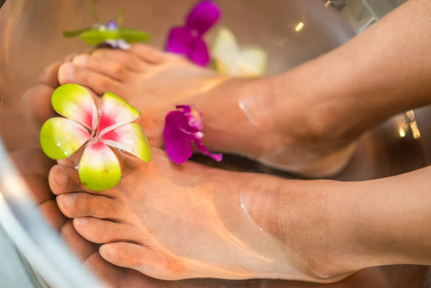 Pieds dans un bain de pieds aux fleurs avant une pédicure